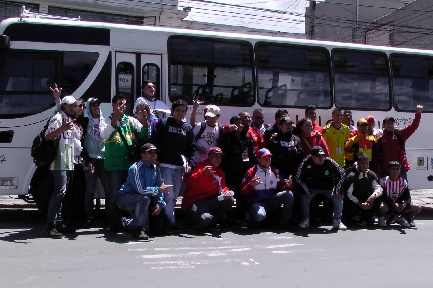 25 young people from 18 fan clubs and the FJMBN stand together in front of a white bus for a group photo.