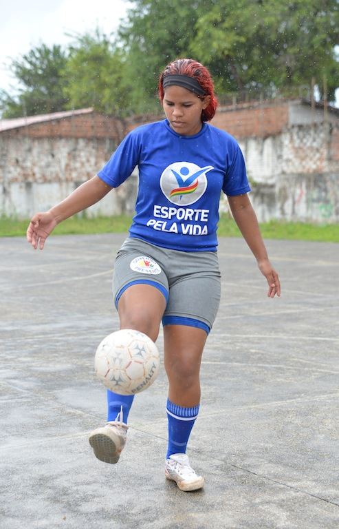 A teenager juggles a white football with her foot.