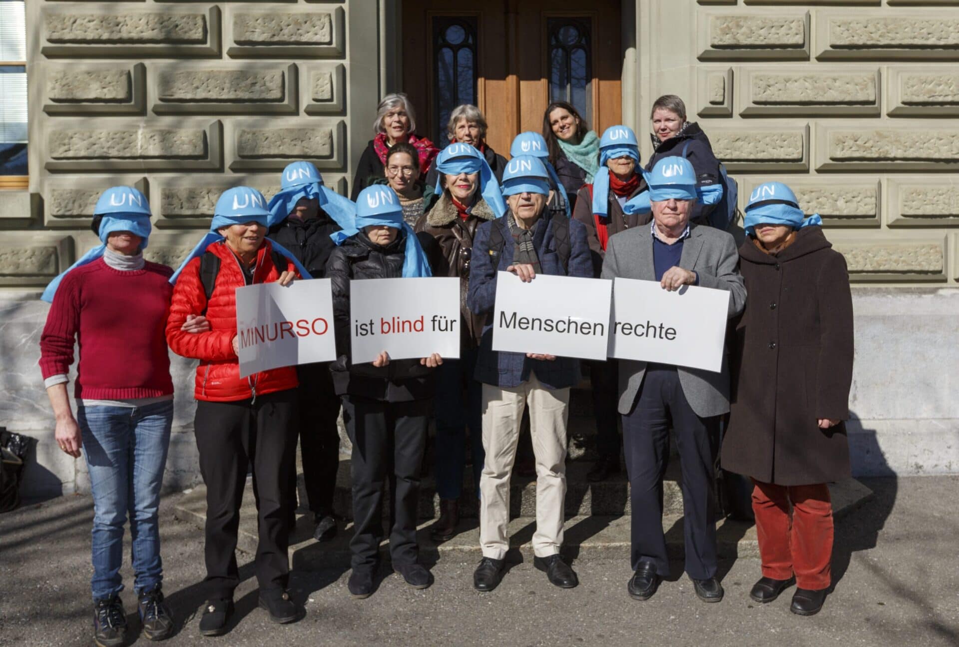 People with blue helmets bearing the UN logo stand together for a group picture in front of the Federal Chancellery.