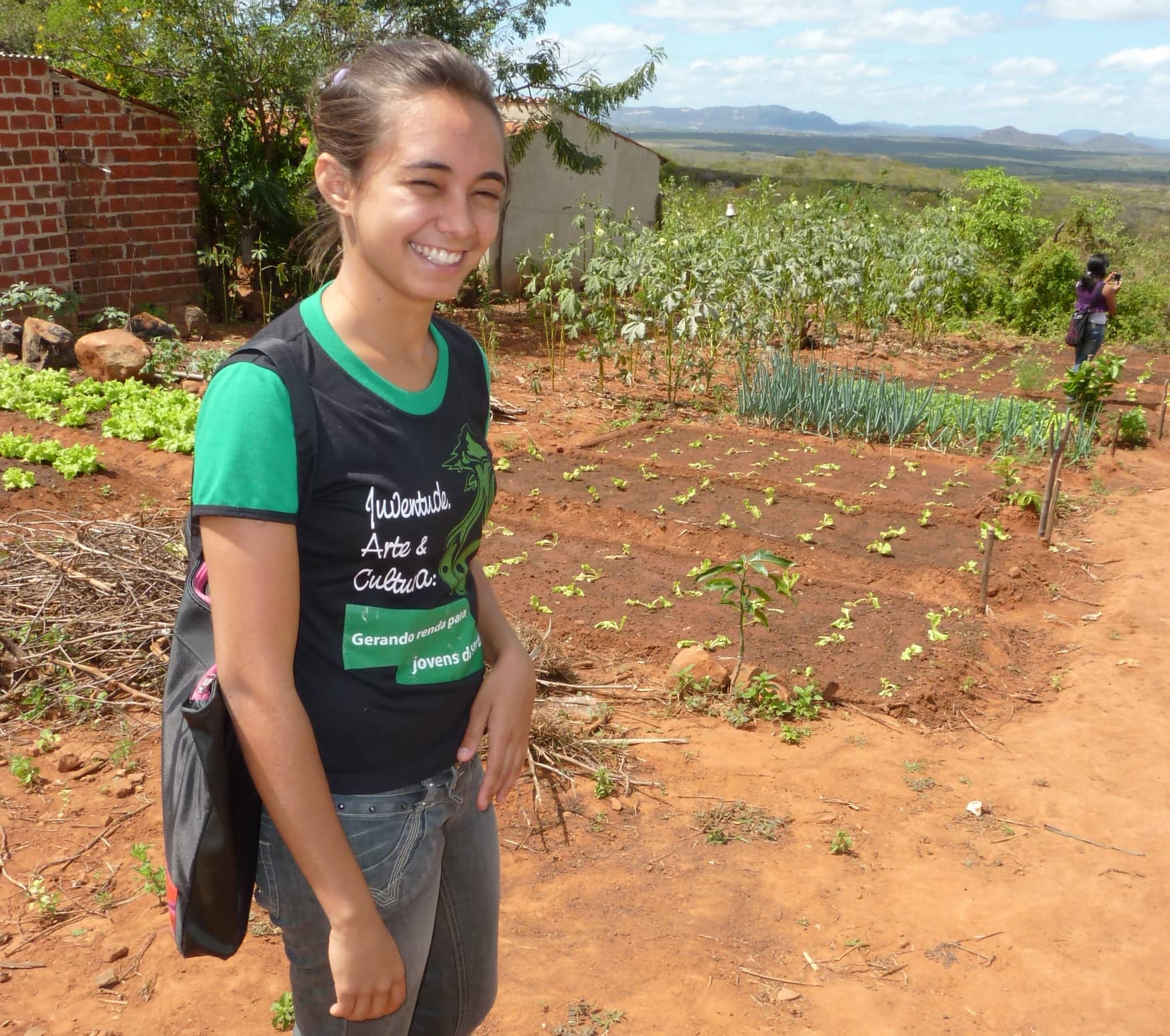 A young woman stands happily in front of her vegetable garden.