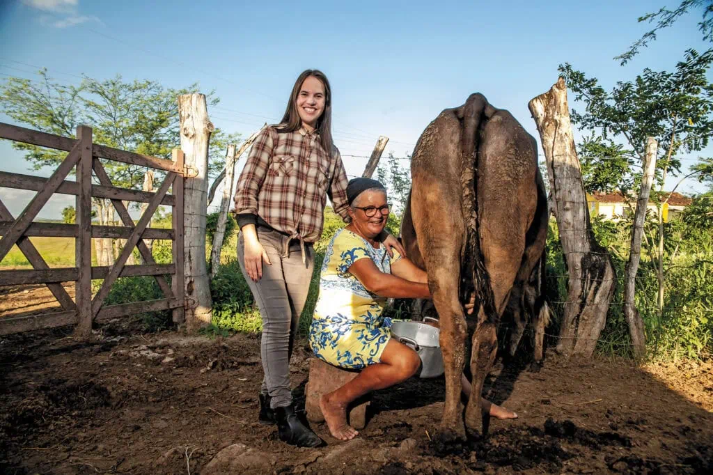 Young-cheerful-woman-with-older-woman-milking-a-cow